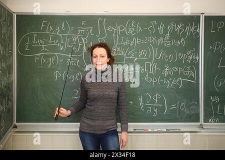 L'insegnante con puntatore si trova vicino alla lavagna con formule matematiche in classe scolastica Foto Stock