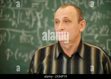 Il vecchio insegnante sta in piedi e guarda lontano vicino alla lavagna in classe scolastica, poco profondo dof Foto Stock