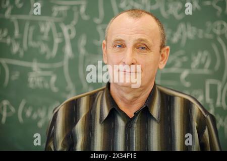 Il vecchio insegnante si trova vicino alla lavagna in classe, poco profondo dof Foto Stock