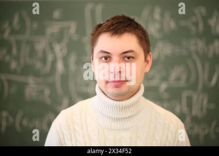 L'insegnante in bianco si trova vicino alla lavagna con formule matematiche in classe Foto Stock