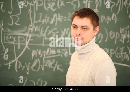 L'insegnante si trova vicino alla lavagna con formule matematiche in classe scolastica Foto Stock