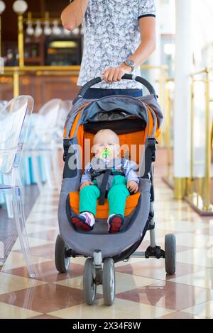 Un bambino carino si siede nel passeggino e le mani del padre nella cornice del ristorante Foto Stock