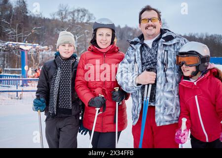 La famiglia di quattro persone si erge sugli sci presso la stazione sciistica di sera. Foto Stock