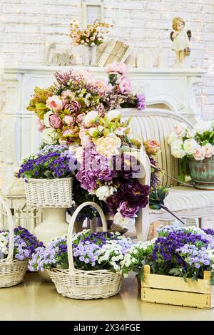 Interno della camera con caminetto, divano e una massa di fiori in pentole, cesti di vimini, scatole di legno. Foto Stock