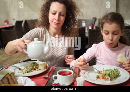 Madre e figlia mangiano insalata e bevono tè a un tavolo in un ristorante Foto Stock