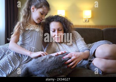 Madre e figlia giocano con un gatto su un divano in camera Foto Stock