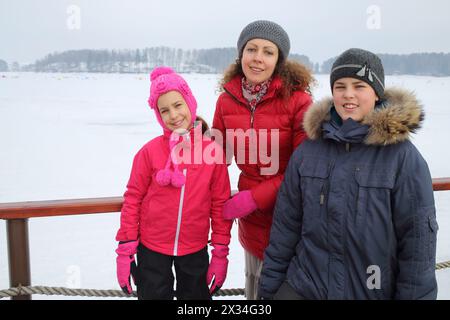 Madre con figlio e figlia in piedi sul molo vicino allo stagno coperto di neve Foto Stock