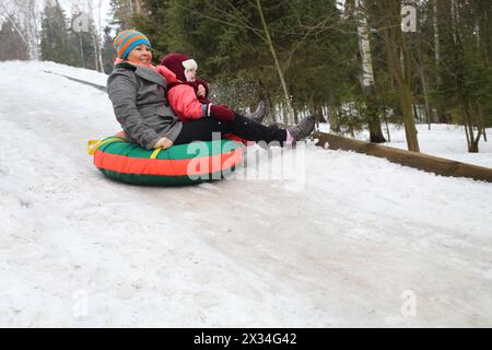 Donna con bambini che rotolano sulle colline su una slitta nella foresta Foto Stock