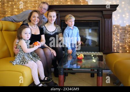 Due genitori con tre bambini in abiti eleganti seduti su un divano vicino al caminetto Foto Stock