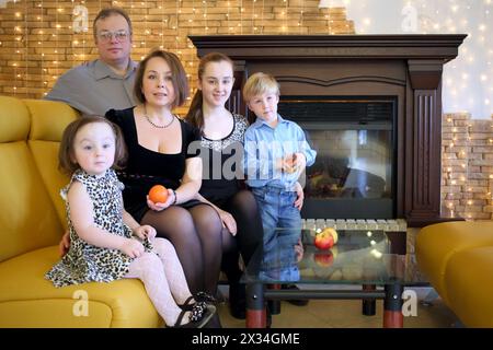 Due genitori con tre bambini in abiti eleganti seduti su un divano vicino al caminetto. Ritratto di famiglia Foto Stock