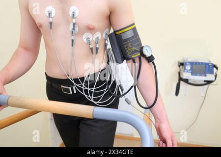 Paziente con elettrodi ECG sul torace e uno strumento per la misurazione della pressione sanguigna durante l'esercizio fisico Foto Stock