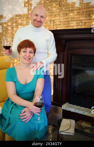 Ritratto di una donna felice e di un uomo con bicchieri di vino vicino al camino Foto Stock