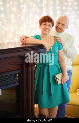 Donna felice con un vestito verde e un uomo in piedi vicino al camino Foto Stock