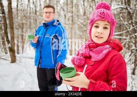 Giovane con occhiali e ragazza in piedi tenendo tazze con tè caldo nel parco innevato, concentrati sulla ragazza. Foto Stock