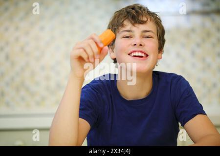 Ragazzo felice in camicia blu scuro che mangia carote pulite, vista ravvicinata Foto Stock