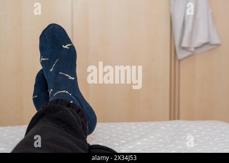 I piedi dell'uomo attraversati ai margini del letto, rilassandosi in camera, belle calze blu. Foto Stock