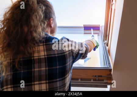 Lavori domestici e stile di vita domestico. Vista posteriore della donna che lava le finestre nel suo appartamento. Foto Stock