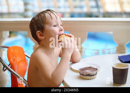 Bambino che mangia un panino e un budino di cioccolato in un caffè del parco acquatico Foto Stock