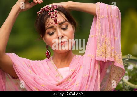 Donna di mezza età in sari rosa e adornamento indiano posa nel parco estivo Foto Stock