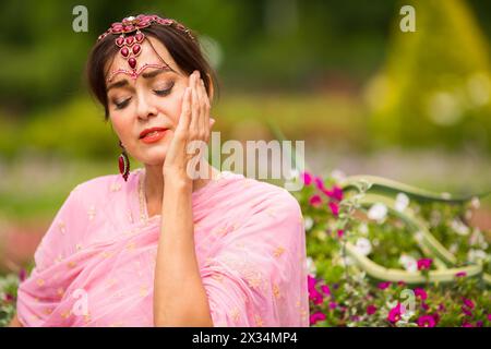 Donna di mezza età in sari rosa e adornamento indiano che si gode nel parco estivo Foto Stock