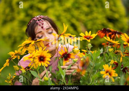 Donna di mezza età in sari rosa e decorazioni indiane odorano fiori nel parco estivo Foto Stock