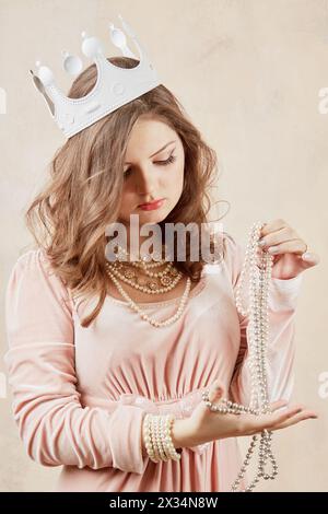 Giovane donna in abito rosa con collana di perle, perline e corona sulla testa. Foto Stock