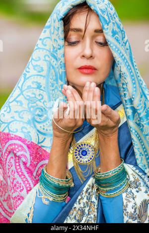 Donna di mezza età in sari blu e adornamento indiano posa in giardino Foto Stock