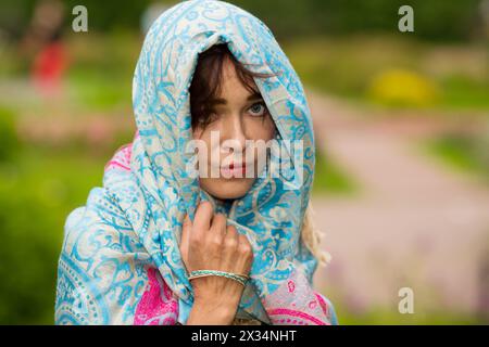 Una donna indiana triste sta in piedi e guarda la macchina fotografica in un luminoso sari in giardino Foto Stock