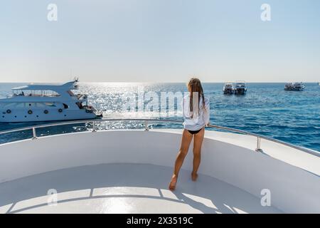 Una bambina di nove anni in una tunica bianca con trecce si siede sul ponte di uno yacht. Foto Stock
