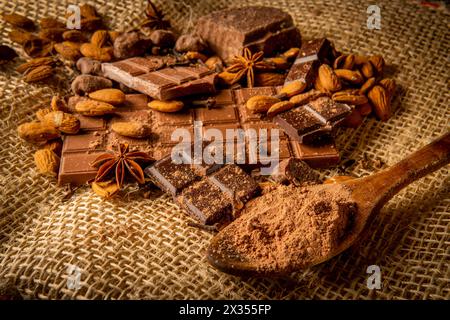 Natura morta di diversi tipi di cioccolato con mandorle e spezie come anice stellato e chiodi di garofano su un sacco Foto Stock