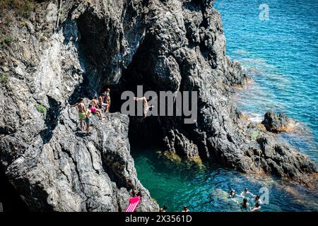 Monterosso, Italia - 10 luglio 2023: Gruppo di persone che si divertono a nuotare e a saltare dalle rocce al mare Foto Stock