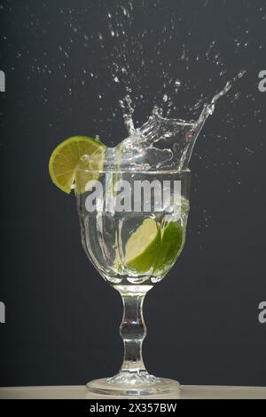 Il limone cade in un bicchiere d'acqua trasparente causando schizzi verso l'alto. Foto Stock