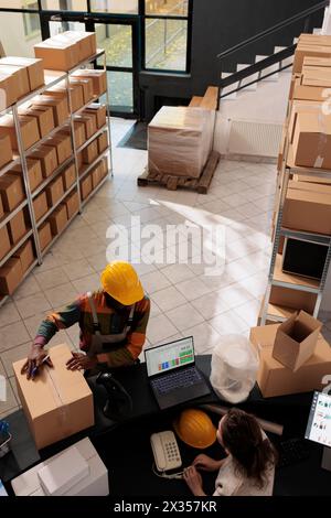 Dipendenti diversi che si trovano al banco di vendita in magazzino, preparando l'ordine del cliente per la consegna. I colleghi del magazzino discutono del controllo di qualità delle merci e lavorano nell'inventario in magazzino Foto Stock