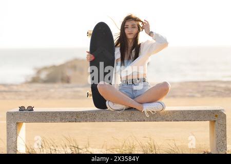 Una donna è seduta su una panchina con uno skateboard in mano Foto Stock