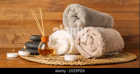 Composizione spa con candele accese, asciugamani, pietre da massaggio e diffusore di aroma su tavolo in legno Foto Stock