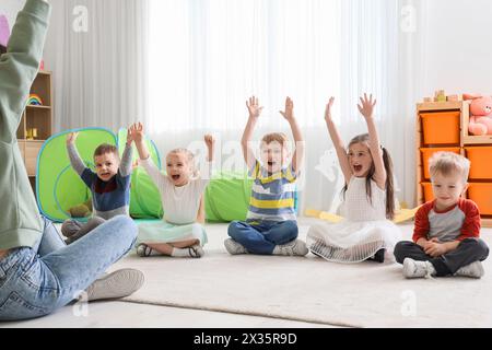 Bambini piccoli con insegnante di asilo che alzano le mani all'asilo Foto Stock