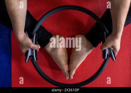 Vista dall'alto della donna latinoamericana (38) che fa esercizi tonificanti con l'anello di esercizio sul tappetino rosso per il fitness. Fondo blu. Studio yoga Foto Stock