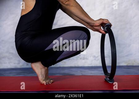 Donna latinoamericana (38) che fa pilates esercizi, tonifica e allunga il suo corpo con un anello di esercizio su un tappetino rosso. Studio yoga o a casa. Foto Stock