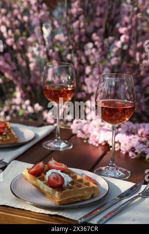 Deliziosi waffle belgi con fragole fresche e vino serviti sul tavolo in giardino Foto Stock