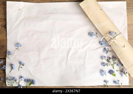 Bellissimi fiori e fogli di carta pergamena vecchia su un tavolo di legno, vista dall'alto Foto Stock