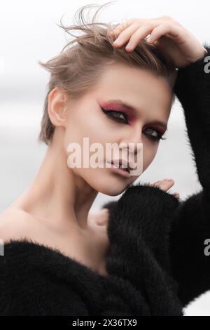 Ritratto la splendida donna bionda è la quintessenza della sensualità. Indossa capelli corti e trucco luminoso e viene posta all'aperto contro il bac naturale bianco Foto Stock