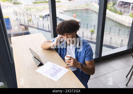 Un giovane uomo birazziale che indossa le cuffie, che esamina i grafici sul tablet Foto Stock