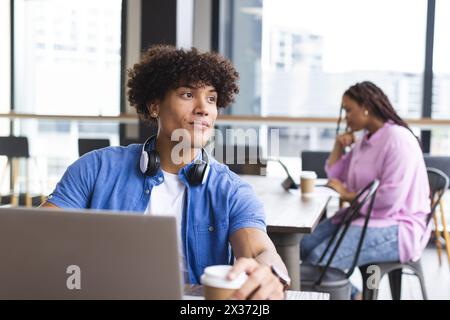 L'uomo birazziale con i capelli ricci usa un laptop in ufficio, una donna in background Foto Stock