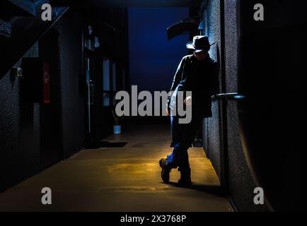 Silhouette di un uomo appoggiato a un muro in un vicolo buio di notte. Concetto di depressione e solitudine. Foto Stock