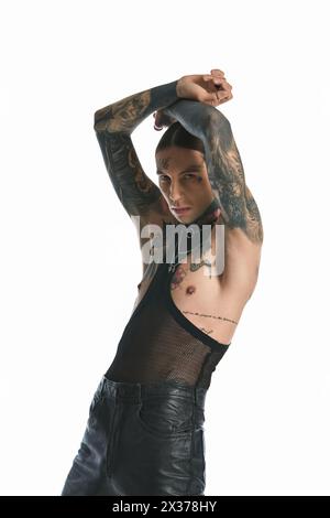 Un giovane uomo elegante con tatuaggi si mette in posa in uno studio su uno sfondo grigio. Foto Stock
