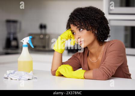 Annoiato, pulito e pensato con una donna nera in cucina di casa per le faccende delle pulizie. Panno, guanti e spray con persone infastidite o frustate Foto Stock