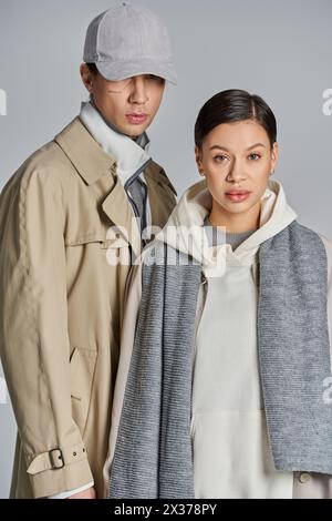 Una coppia giovane ed elegante che indossa un trench in piedi insieme in uno studio su uno sfondo grigio. Foto Stock