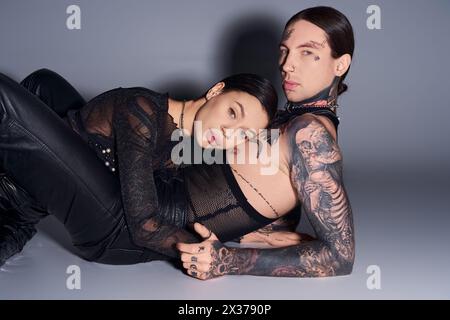 Una giovane coppia tatuata si mette in posa in uno studio su uno sfondo grigio. Foto Stock