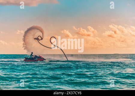 Silhouette di un pilota di fly board in mare. Il pilota professionista fa dei trucchi nella laguna blu. Attrezzature per sport acquatici tropicali. Vista mare al tramonto, estate all'aperto Foto Stock