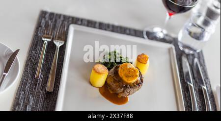 Delizioso filetto di maiale smaltato per cena con contorno rosmarino su piatto bianco, raffinata cucina gourmet primo piano, cipolla smaltata balsamica, guarnita Foto Stock